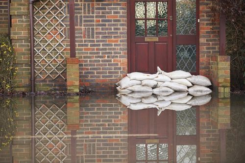 Image is of a wooden door with sand bags in front to keep flood waters away concept of water-damaged wooden door