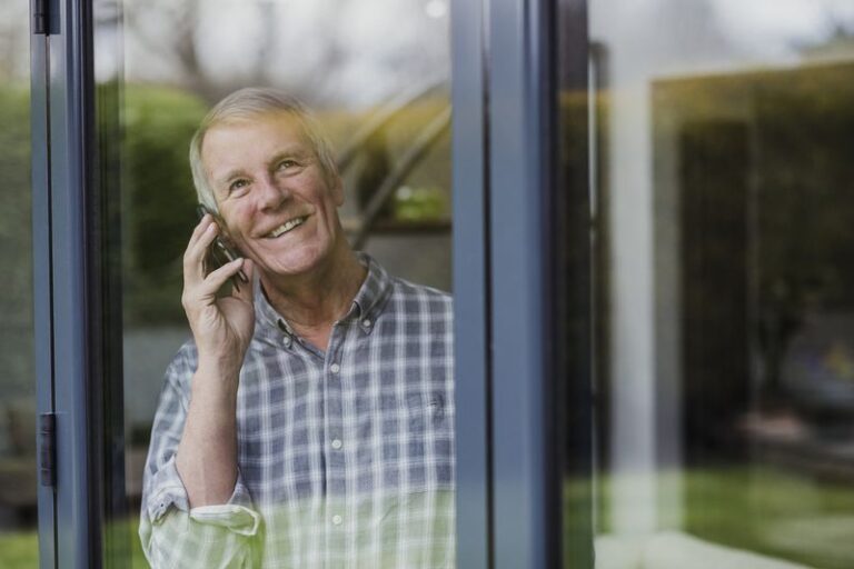 Image is of an older man enjoying a phone conversation while looking out of his new sliding glass doors.