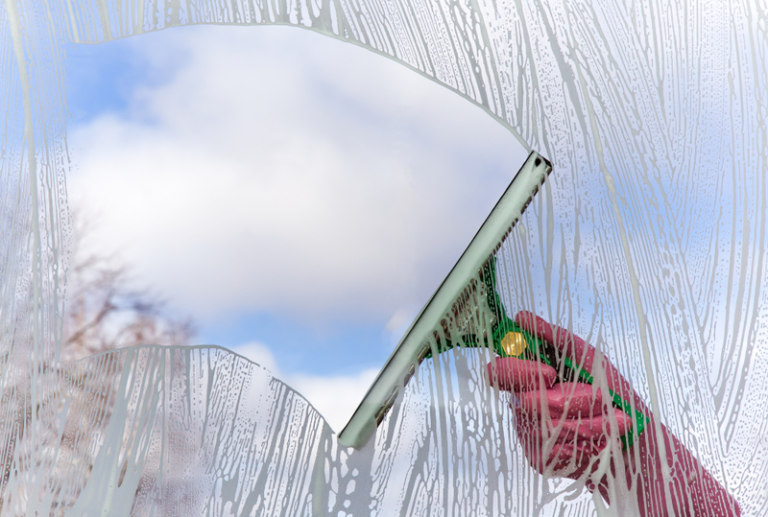 Image is of a hand cleaning a window with a squeegee, concept of clean window checklist in Spring