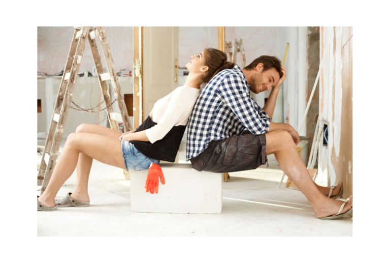 Image is of a couple leaning their backs up to one another, tired and overwhelmed in a house that is under construction. Concept of common DIY window installation pitfalls