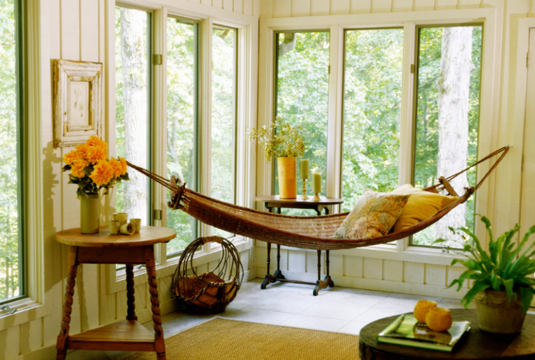 Image is of a sunroom with lots of windows and a hammock hanging surrounded by potted plants, concept of finding perfect sunroom windows