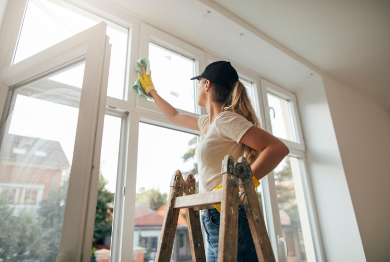 Image is of a woman cleaning her new windows, concept of how long do replacement windows last?